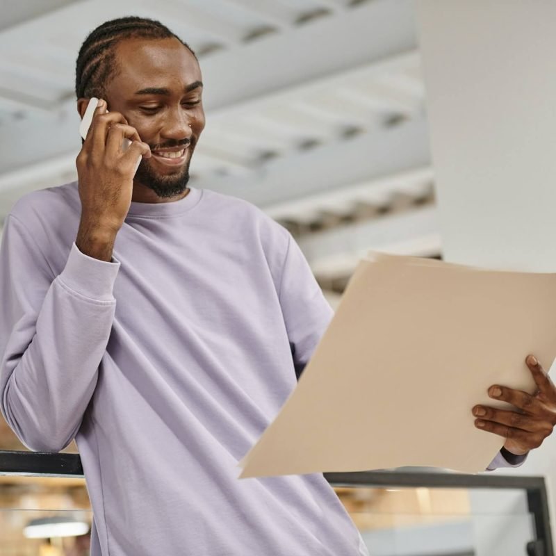happy african american man looking at project on paper talking on smartphone planning startup